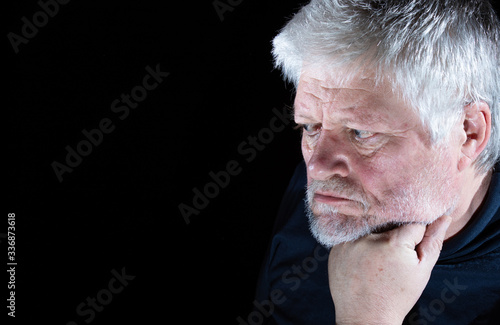 Portrait of an older man. He sits idly in the dark, resting his head on one hand.