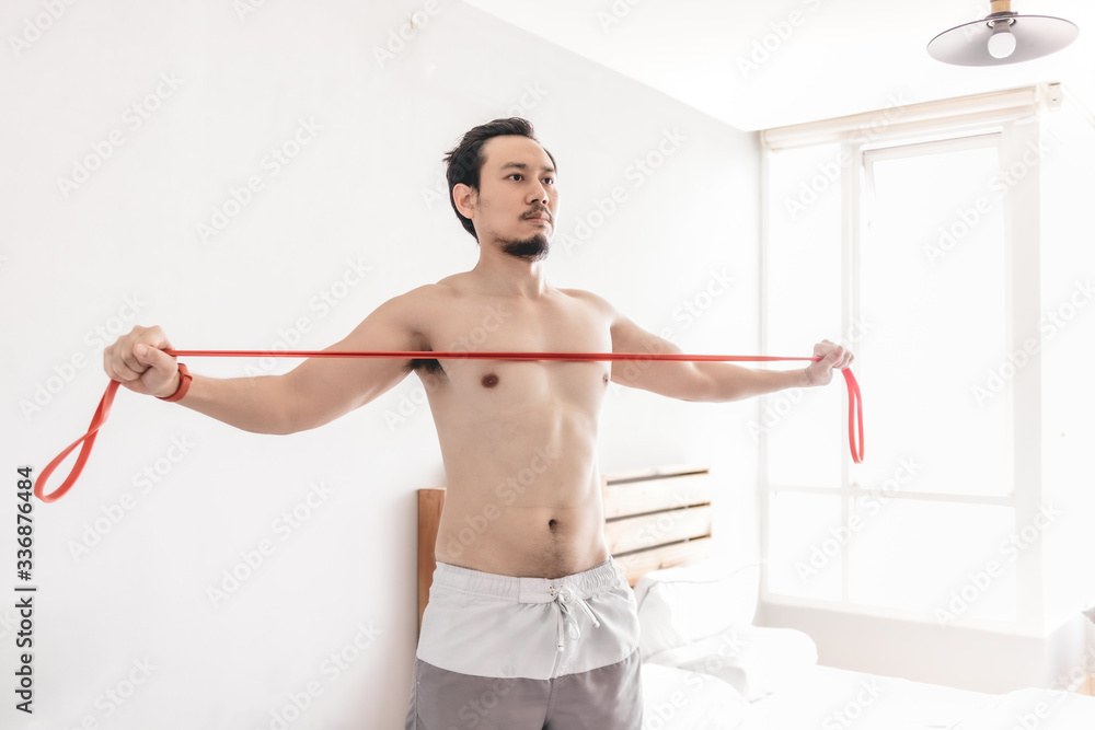 Fototapeta premium Asian man stretching his muscle in concept of workout at home with resistance band.
