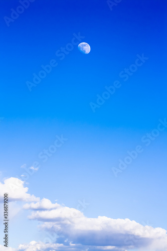 Blue gradient sky with moon and clouds. Vertical background with quarter moon and day sky with cumulus clouds. For smartphones, tablets, banners, invitations