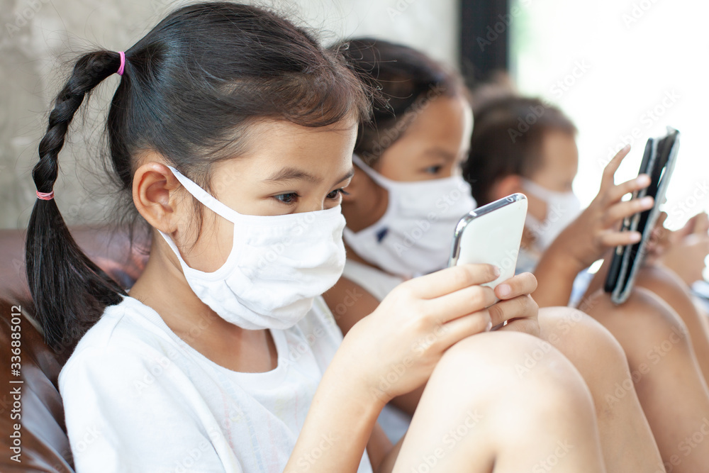 Asian children boy and girls wearing protection mask playing on the smartphone together at home quarantine from the coronavirus Covid-19 and air pollution pm2.5.
