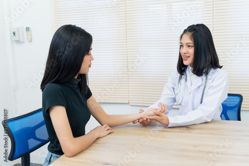 Young Asian female doctor holds adult female patient’s hand to examine and diagnose her sickness and symptom. Medicine and health care concept. Doctor and patient.