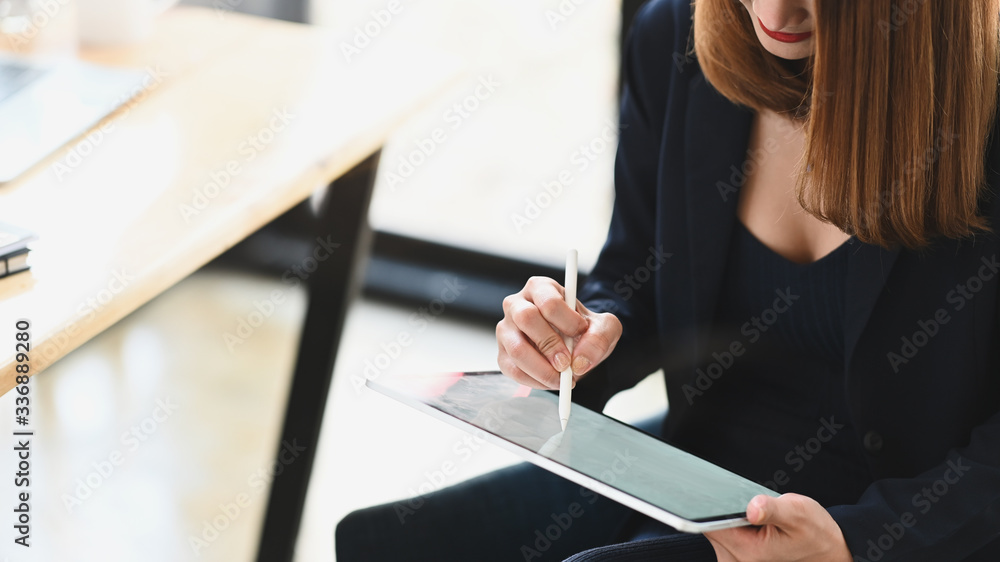 Cropped shot sexy businesswoman holding a computer tablet and stylus pen while sitting at the wooden working desk over comfortable sitting room as background. Cropped shot sexy businesswoman holding a computer tablet and stylus pen while sitting at the wooden working desk over comfortable sitting room as background.
