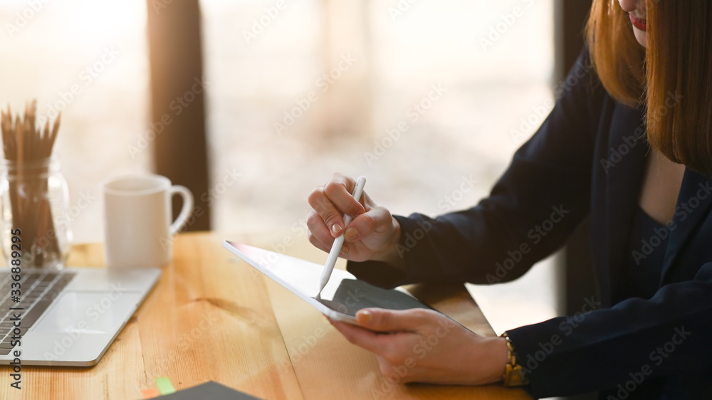 Fototapeta premium Closeup businesswoman holding a computer tablet and stylus pen while sitting at the wooden working desk over comfortable sitting room as background.