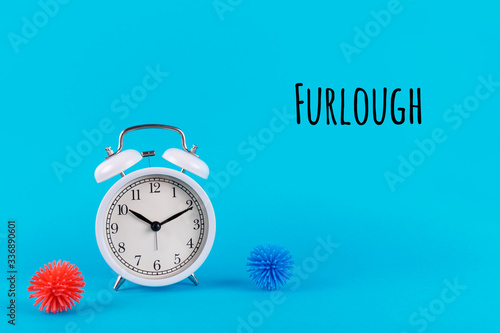 Alarm clock and plastic balls as viruses on the blue background with Furlough wording. Epidemic, social isolation, coronavirus COVID-19 concept. Option with text
