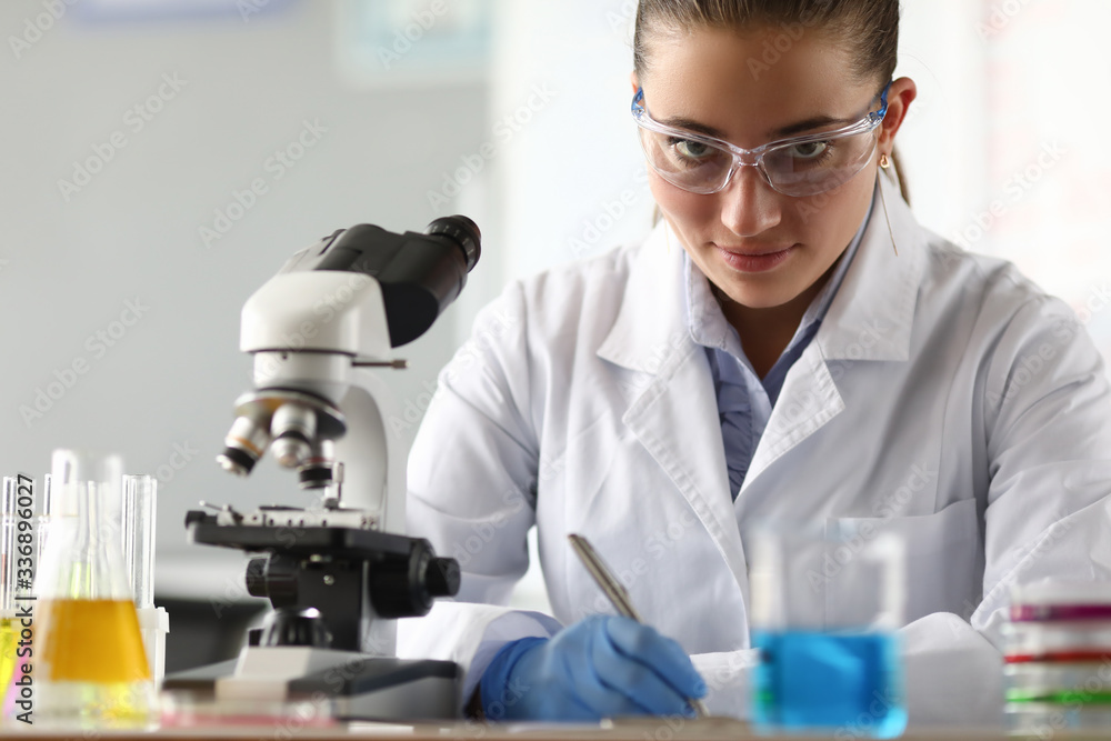 Portrait of serious researcher looking at camera with calmness. Smiling laboratory assistant writing research data in documents. Chemical experiments concept Portrait of serious researcher looking at camera with calmness. Smiling laboratory assistant writing research data in documents. Chemical experiments concept