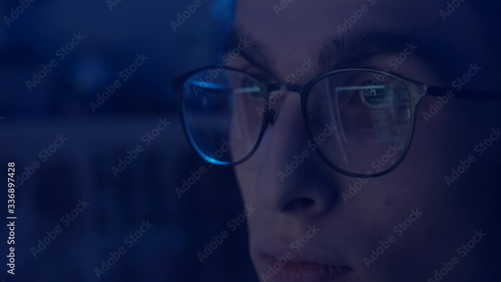 Young man in glasses working at computer, reflection of monitor in glasses, slow motion, shallow depth of field Young man in glasses working at computer, reflection of monitor in glasses, slow motion, shallow depth of field