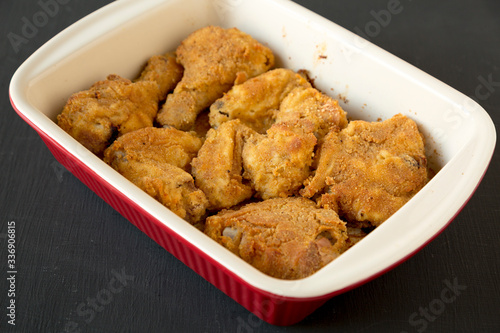 Delicious homemade oven baked fried chicken in a dish on a black surface, top view. Flat lay, overhead, from above. Close-up.