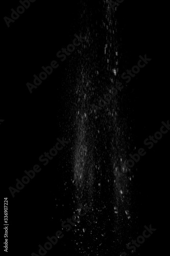 White powder in the form of snow or flour falls from top to bottom isolated on black background