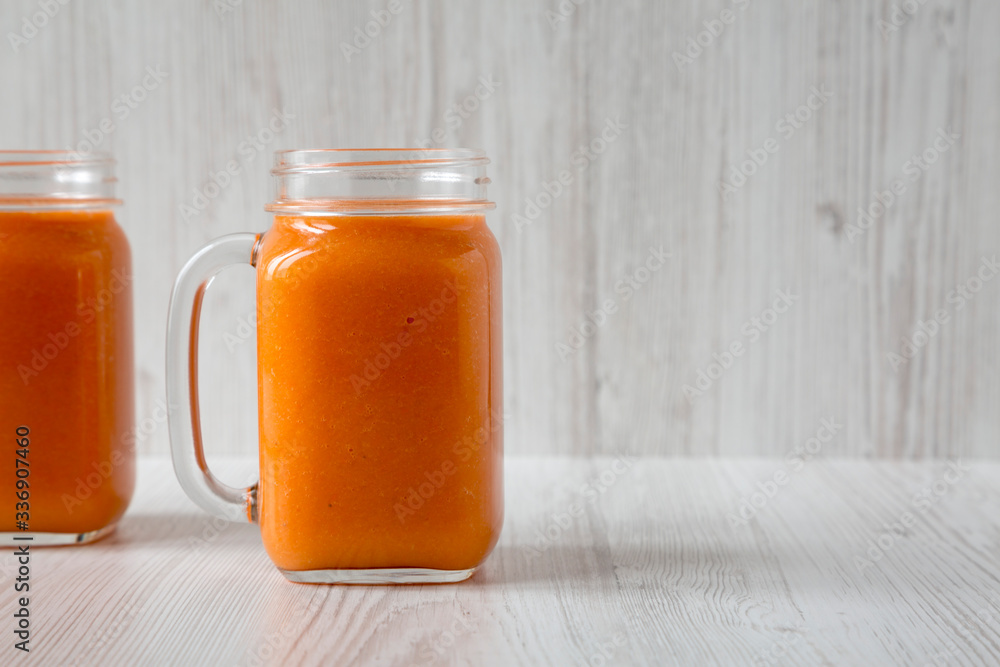 Homemade Mango Carrot Smoothie in a glass jar mug over white wooden surface, side view. Copy space. Homemade Mango Carrot Smoothie in a glass jar mug over white wooden surface, side view. Copy space.