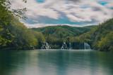Long exposure view of the Gavanovac waterfall in Plitvice lakes, Croatia on a cloudy spring day. Small flowing waterfall surrounded by trees and roots in springtime. Fairytale landscape.