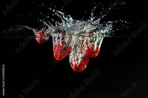Falling strawberries into the water, spray for design, freezing in motion. Water splash and vegetables isolated on a black backgroud