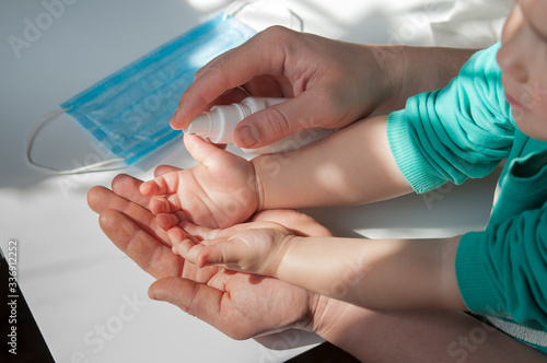close-up of hand disinfection of an adult child with a bottle of antiseptic on the table a medical mask
