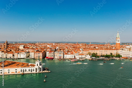 Aerial shot of Venice city and Grand Canal, Italy. View from above. Tiled roofs and nerros streets. Venetian atmosphere. Blue sky and lagoon water. Historical buildings. © Artem