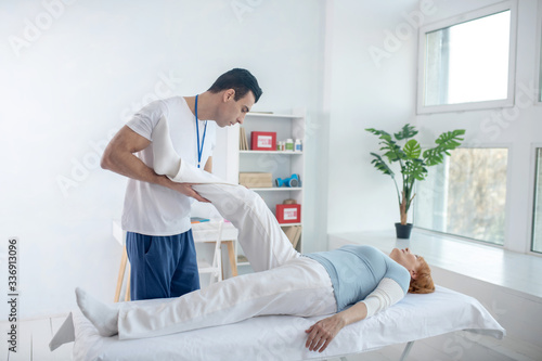 Nice professional therapist lifting his patients leg