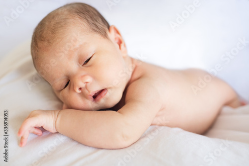 Newborn baby boy lying and sleeping on white bed at home