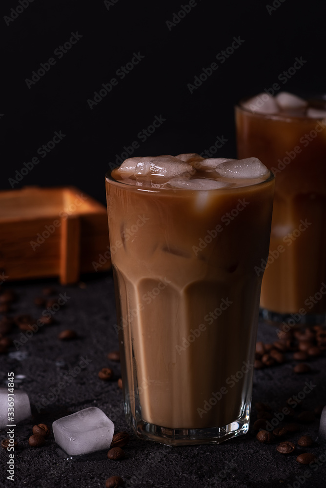 Iced coffee in a tall glass with cream poured over. Wood background. Low key. Iced coffee in a tall glass with cream poured over. Wood background. Low key.
