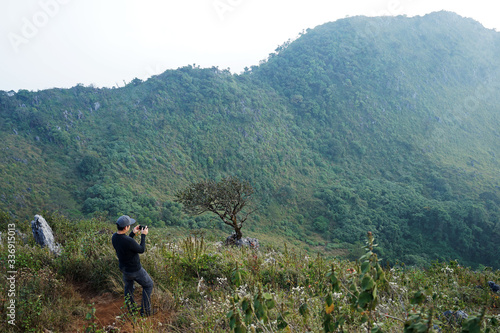 A man on the peak taking a photo of green mountain range with cloudy sky