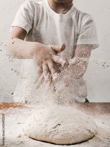 Crop unrecognizable child person clapping hands with flour while cooking bread sprinkling white flour over blob of dough. Vertical. Copy space bottom