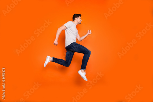 Full length profile photo of attractive crazy youngster jump high rush sale shopping center addicted shopper wear striped t-shirt jeans shoes isolated bright orange color background