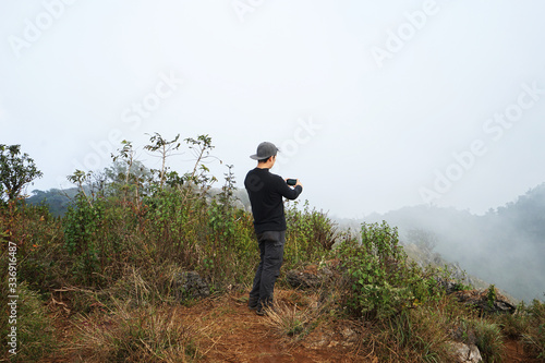 A man on the peak taking a photo of green mountain range with cloudy sky