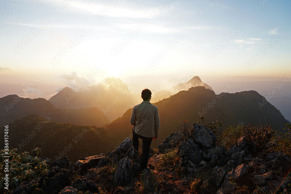 A man standing on the peak looking at green mountain range with cloudy sky