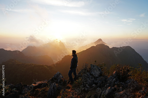 A man standing on the peak looking at green mountain range with cloudy sky