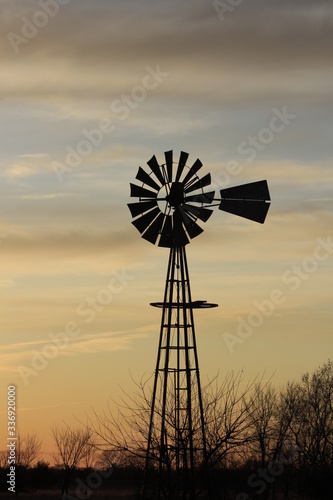 Kansas Windmill silhouette at Sunset with a tree out in the country north of Hutchinson Kansas USA.