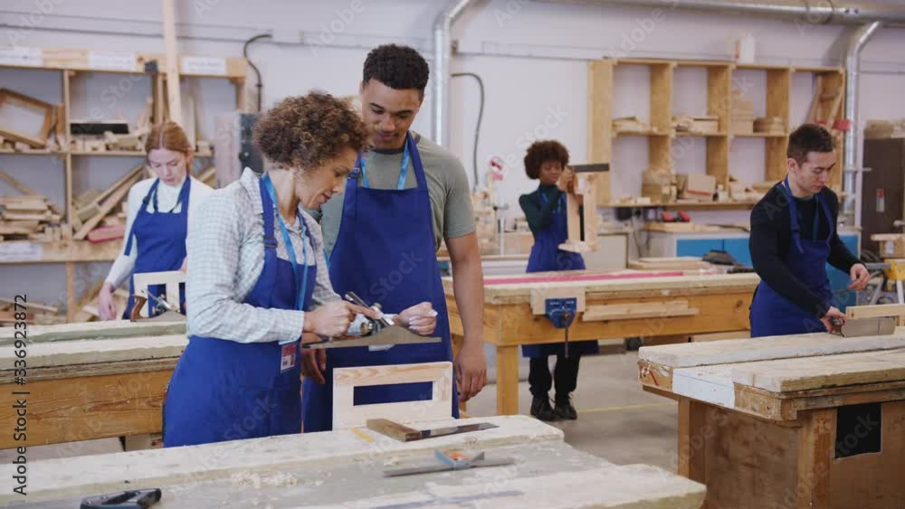 Dolly shot of female tutor with carpentry student in workshop studying for apprenticeship at college using wood plane - shot in slow motion Dolly shot of female tutor with carpentry student in workshop studying for apprenticeship at college using wood plane - shot in slow motion
