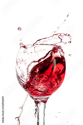 Splash of falling red wine in a round glass on a white background