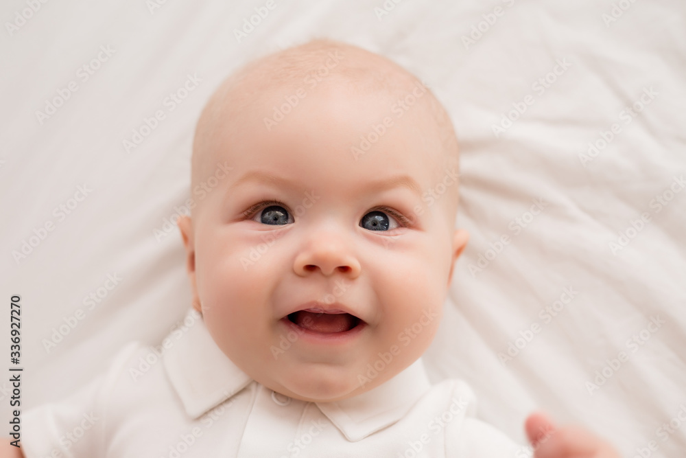 Healthy toddler boy smiling in white clothes lies on the bed view from above