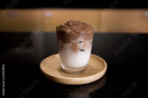 Iced Dalgona Cocoa / Chocolate, a creamy whipped cocoa, on wooden tray on black table. 