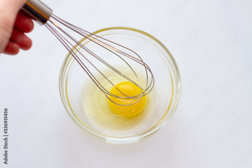 hand whipping egg white with a metal whisk in a glass bowl hand whipping egg white with a metal whisk in a glass bowl