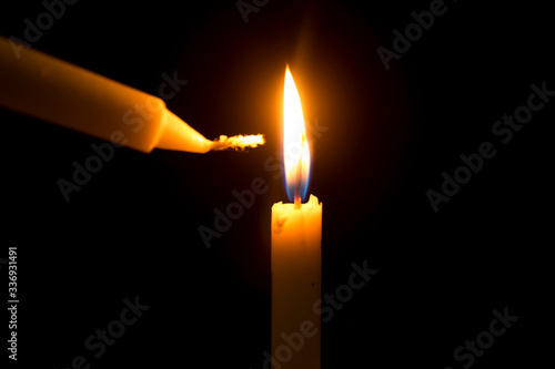 Burning a candle with another candle in the dark room.