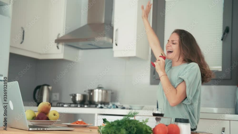 Young caucasian cheerful woman having fun while cooking in the kitchen and talking with friends via the internet. Young caucasian cheerful woman having fun while cooking in the kitchen and talking with friends via the internet.
