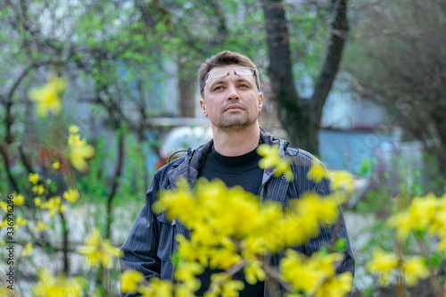 Portrait of brunette man, enjoying the view of spring yellow flowers on the street.  © elenakirey
