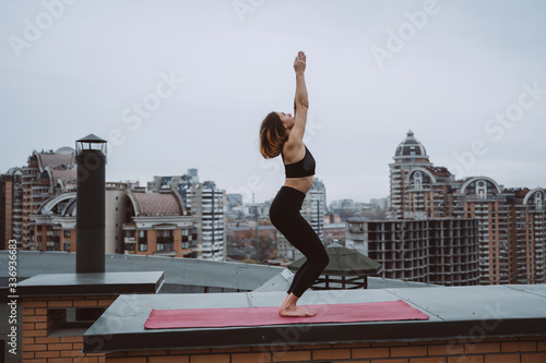 Woman practicing yoga on the mat on the roof and doing yoga exercises