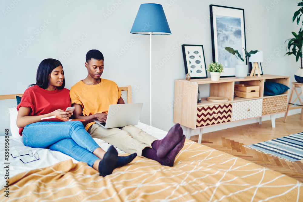 Black woman with smartphone and book talking with boyfriend with laptop Black woman with smartphone and book talking with boyfriend with laptop