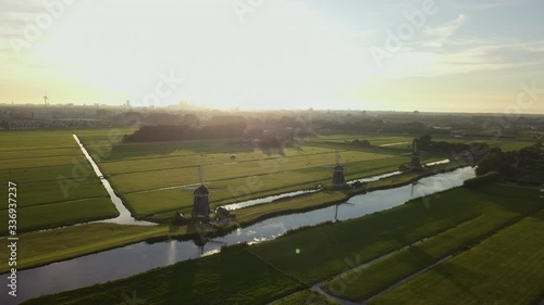Aerial shot of three iconic windwills in Wilsveen, the Netherlands, flyign towards them during golden hour over green fields photo