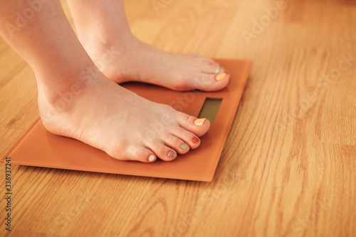 Woman with barefoot standing on the scales on wooden background. Cares about a body. Weight loss concept. Side view