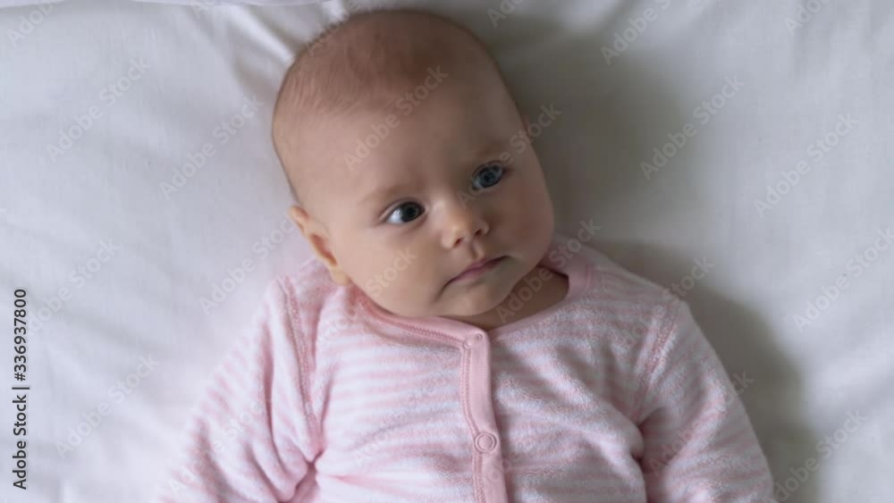 Top view of sweet newborn baby girl lying on bed, curiously looking around Top view of sweet newborn baby girl lying on bed, curiously looking around