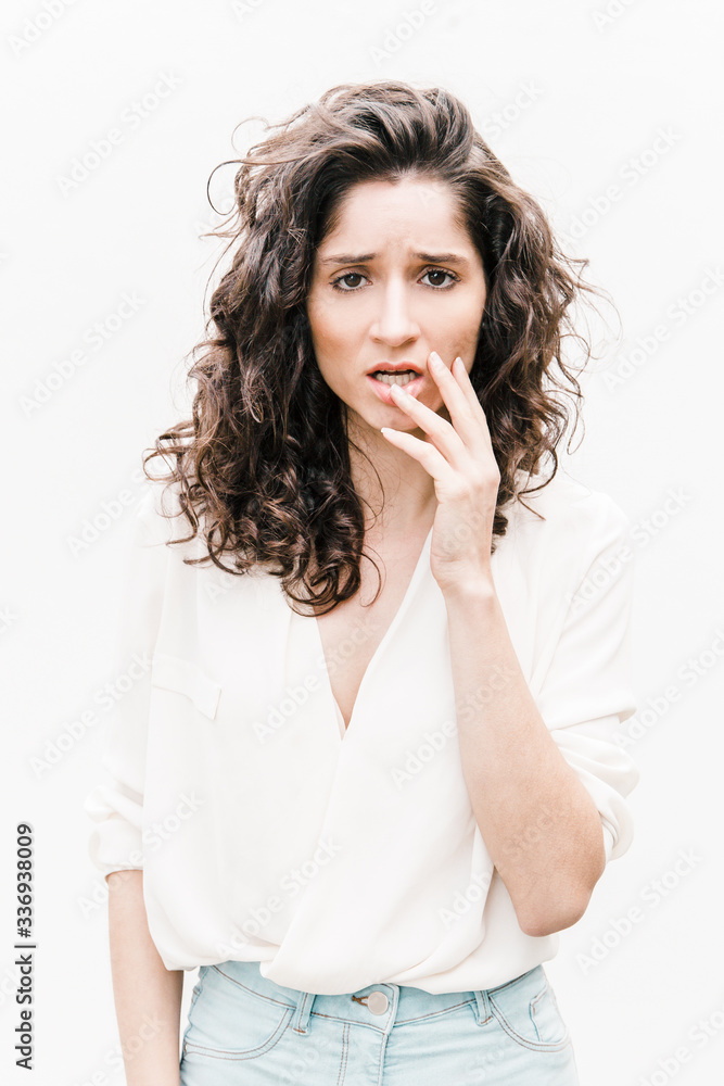 Worried confused woman touching face, realizing mistake. Wavy haired young woman in casual shirt standing isolated over white background. Error or memory problem concept Worried confused woman touching face, realizing mistake. Wavy haired young woman in casual shirt standing isolated over white background. Error or memory problem concept