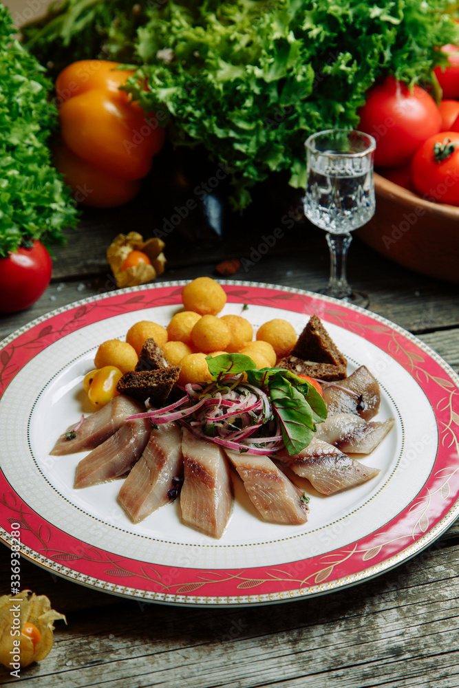 Restaurant dish with vegetable decor on a wooden background. Salted herring cut into slices on a plate.