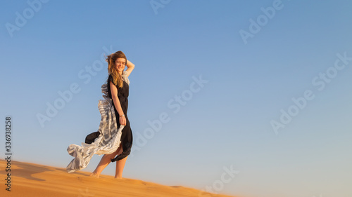 A woman in a black dress with a cloth in her hands in a strong wind alone in the desert. A girl walks on the sand in a deserted desert. © ALEXEY