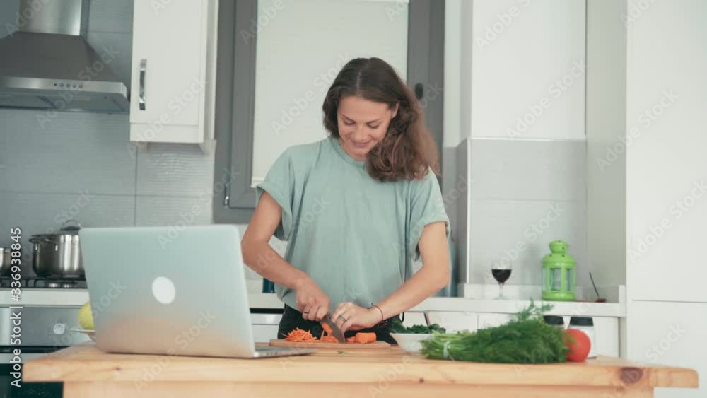 Young caucasian cheerful woman cooking in the bright kitchen while talking with friends via the internet. Cooking classes from a chef. Young caucasian cheerful woman cooking in the bright kitchen while talking with friends via the internet. Cooking classes from a chef.