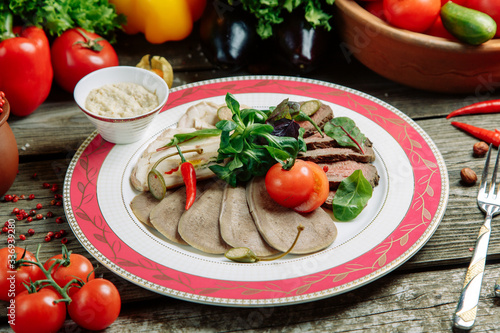 Restaurant dish with vegetable decor on a wooden background. Beef cut-up on a plate with greens.