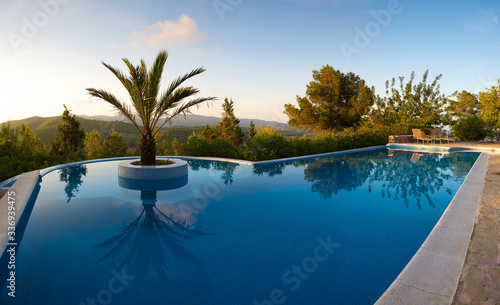 Beautiful swimming pool and palm tree in the center, scenic landscape in Ibiza during the sunset, clear blue sky. Spain 2011