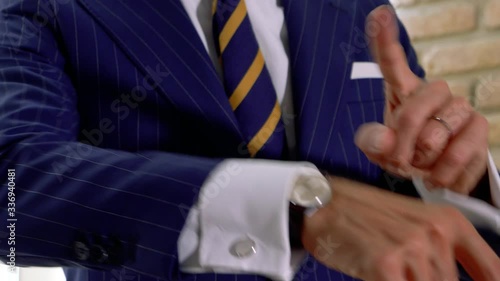 Elegant man dressed in blue pinstripe suit. shows us his cufflinks and his classic watch photo