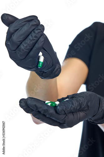 Close-up of hands in black latex gloves of a girl in black, pouring from palm to palm medical capsules of white-green color, isolated on white.