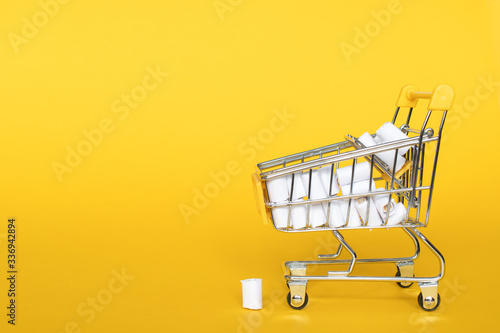 Full grocery cart of toilet paper near of a pyramid of toilet paper rolls banner, place for text, wholesale trade, humor. Delivery, online shopping