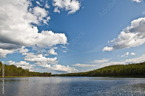 Foto Beautiful volumetric clouds on a sunny day over a quiet forest lake